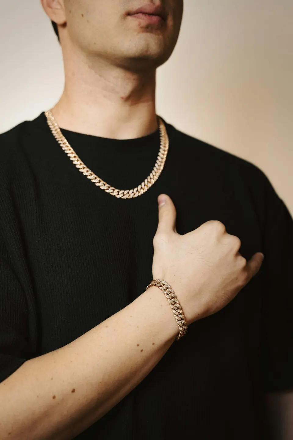 Mann trägt goldene Kette und goldenes Gliederarmband, Detailaufnahme vor violettem Hintergrund