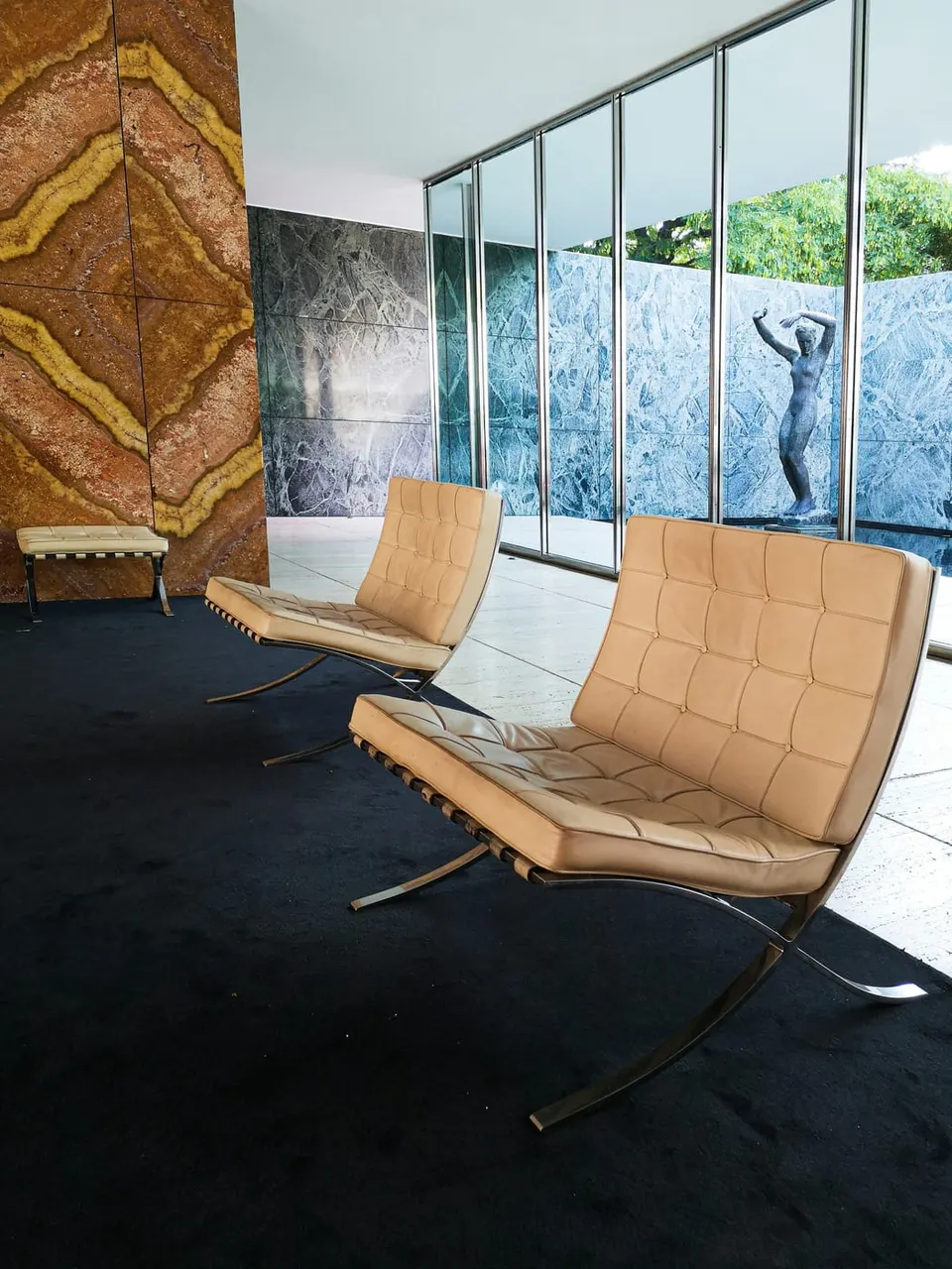 Zwei Barcelona Chairs in hellem Leder vor der Onyxwand des rekonstruierten Barcelona-Pavillons, im Hintergrund die Kolbe-Skulptur am Wasserbecken