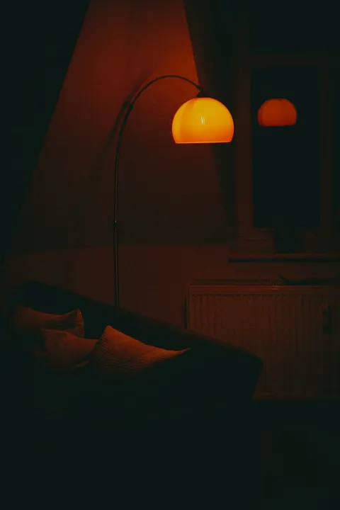Warm leuchtender Kuppelschirm einer Bogenlampe über einem Sofa im abgedunkelten Wohnzimmer