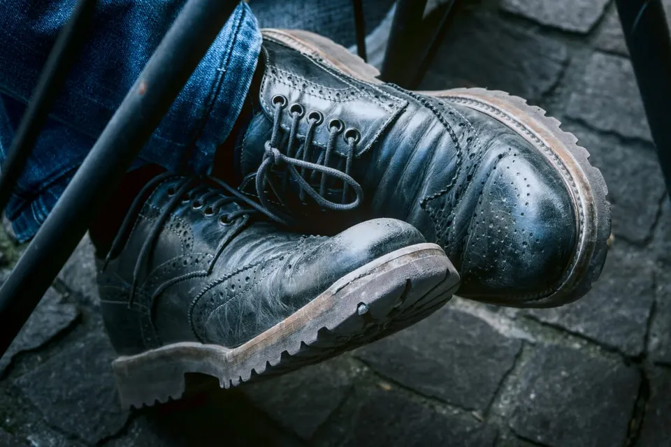 Abgetragene schwarze Brogue-Stiefel mit Patina zu Jeans auf Kopfsteinpflaster