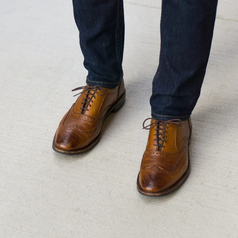 Dunkle Jeans mit Saum zu hellbraunen Brogues mit Flügelkappe, von oben gesehen