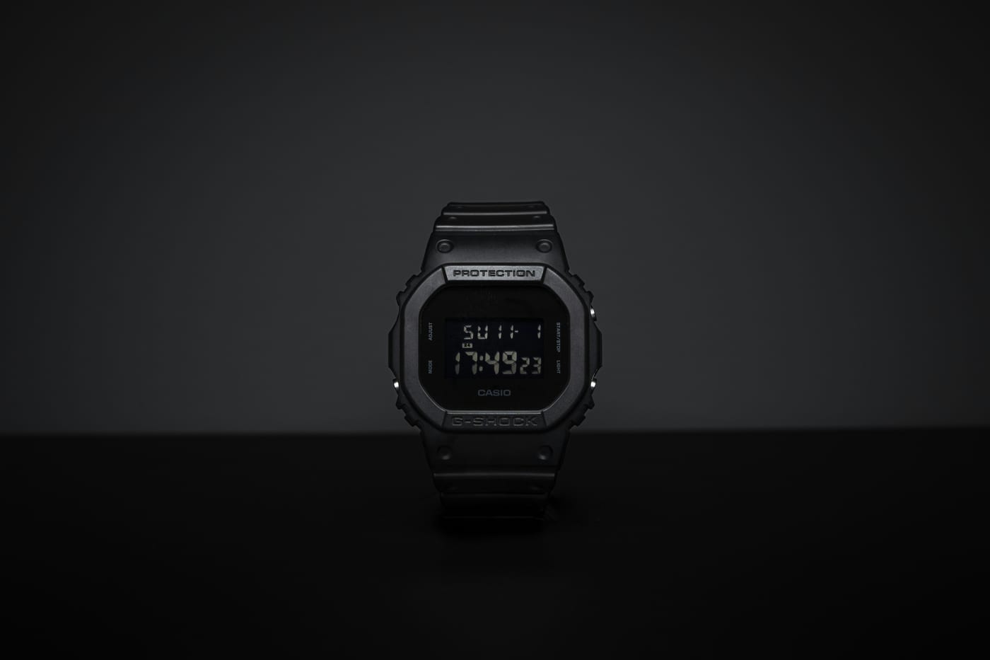 Schwarze Casio G-Shock in der quadratischen 5600er-Form mit Negativdisplay, frontal vor dunklem Hintergrund