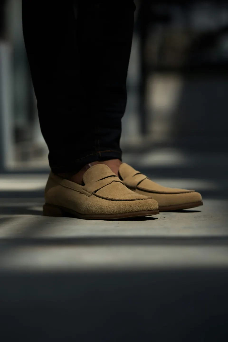 Hellbraune Wildleder-Penny-Loafer ohne Socken zu dunkler Jeans auf Straßenpflaster