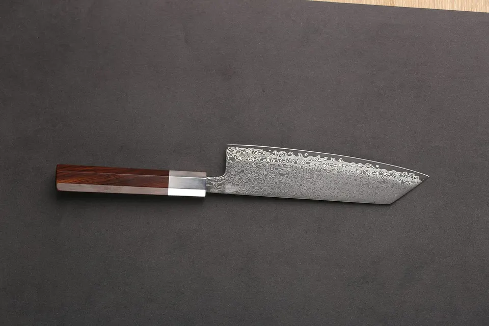 Ein Kiritsuke mit Rosenholzgriff liegt auf dunklem Grund, das Lagenmuster zieht in Wellen über die Klinge und endet oberhalb der Schneide an einem glatten Streifen