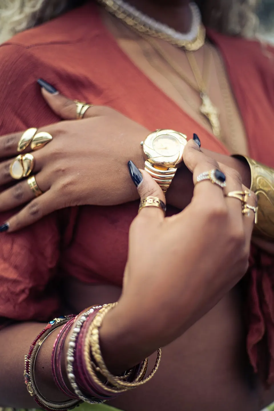 Frauenhand mit mehreren Goldringen, gestapelten Armbändern und einer goldenen Uhr am flexiblen Band