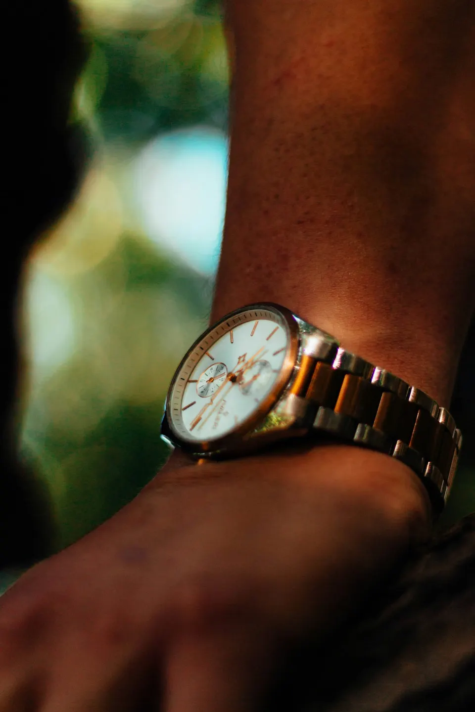 Bicolor-Uhr aus Gold und Stahl am schlanken Handgelenk vor grünem Hintergrund