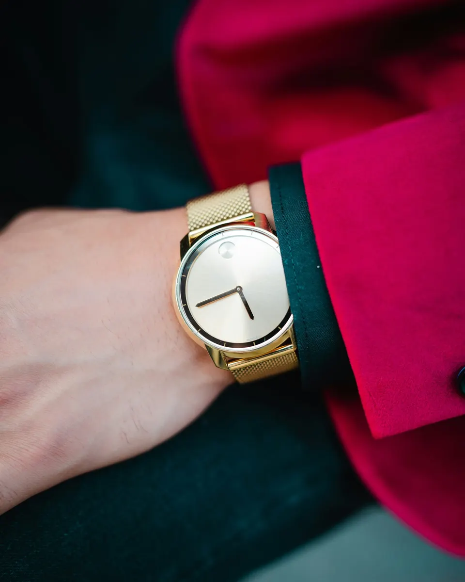 Frauenhandgelenk mit goldener Milanaise-Uhr vor einem magentafarbenen Blazer