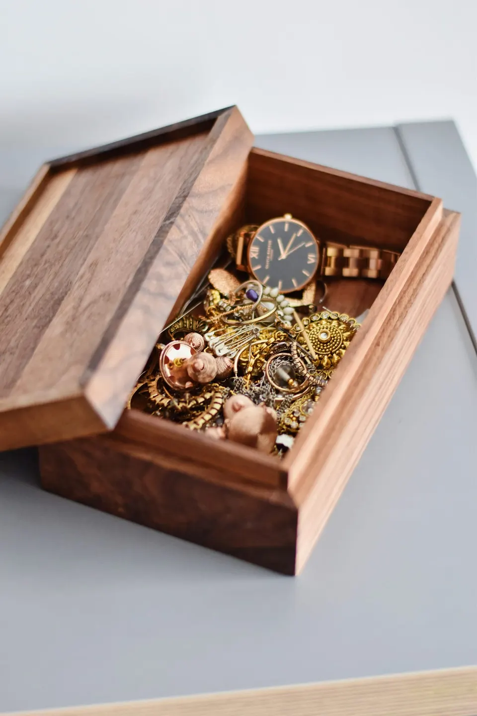 Geöffnete Holzschatulle mit einer goldenen Uhr zwischen Ketten, Ringen und Ohrringen