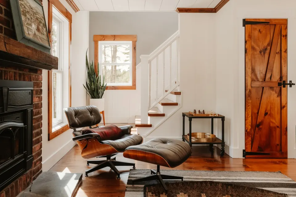Gebrauchter Lounge-Sessel mit Ottoman aus dunklem Furnier und braunem Leder vor einem Backsteinkamin