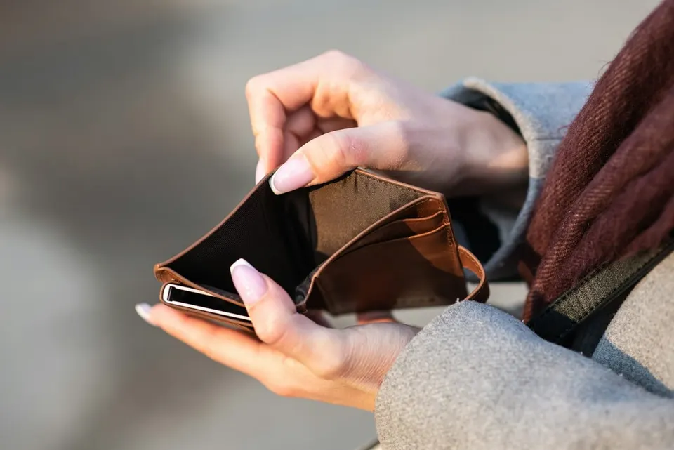 Haende halten eine aufgeklappte Leder-Geldboerse und ein Smartphone
