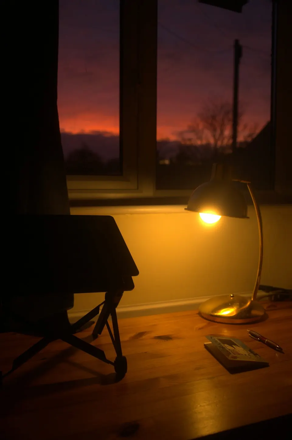 Warm leuchtende Schreibtischleuchte auf einem Holztisch vor einem Fenster mit Abendhimmel