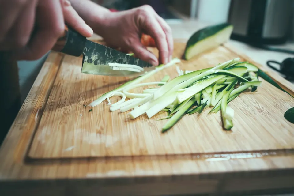 Ein Santoku mit Hammerschlag schneidet eine Gurke auf einem Holzbrett in feine Streifen
