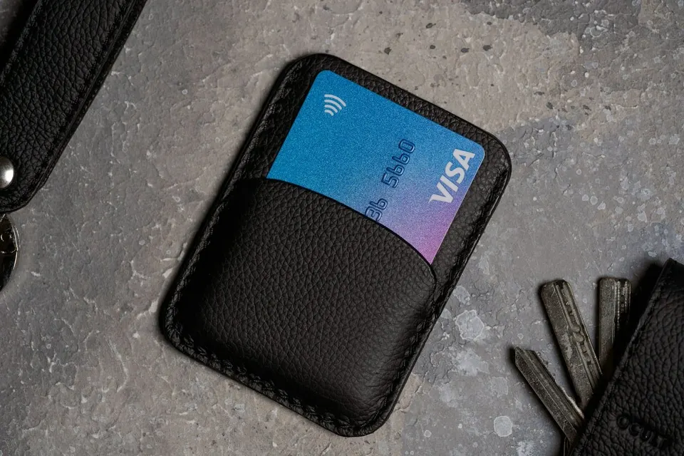 Schwarzes Kartenetui mit Bankkarte neben Schluesseln auf dunkler Flaeche