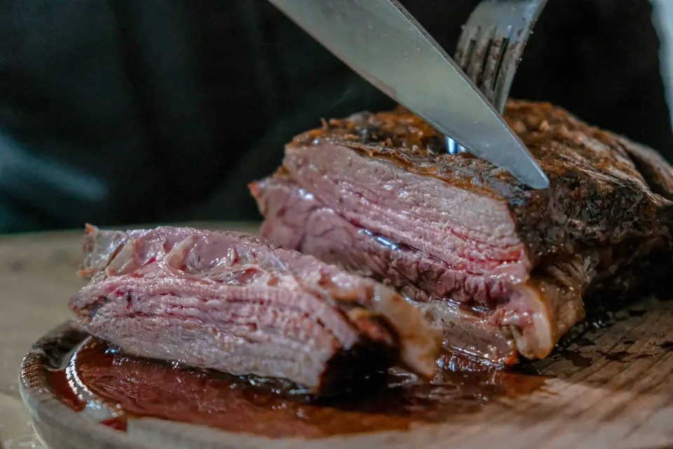 Rosa gebratenes Rindfleisch wird mit einem langen Messer und einer Gabel in Scheiben geschnitten