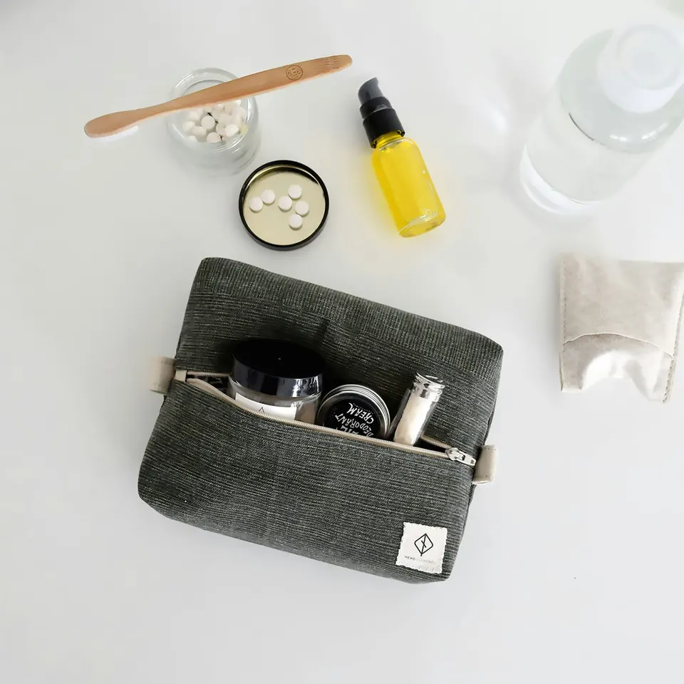 Kompakte graue Kulturtasche von oben, daneben Reisegrößen, eine Zahnbürste aus Holz und eine kleine gelbe Flasche