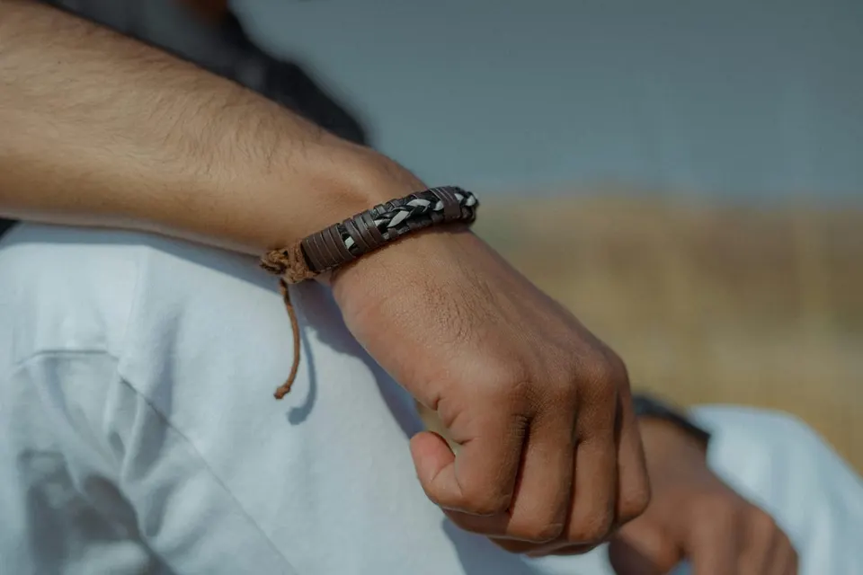 Geflochtenes braun-schwarzes Lederarmband mit Schiebeknoten am Handgelenk eines Mannes im weißen Shirt