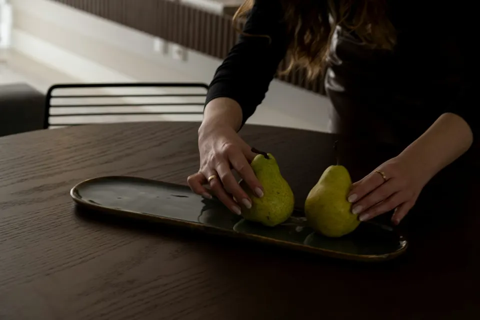Zwei Birnen werden auf einem dunklen ovalen Tablett auf einem dunklen Holztisch zurechtgelegt