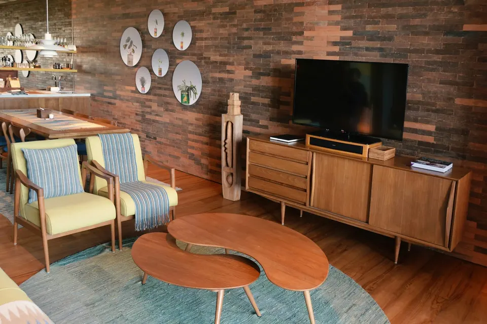 Mid-Century-Wohnzimmer mit zwei biomorphen Nierentischen aus Teak vor Backsteinwand und gestreiften Sesseln