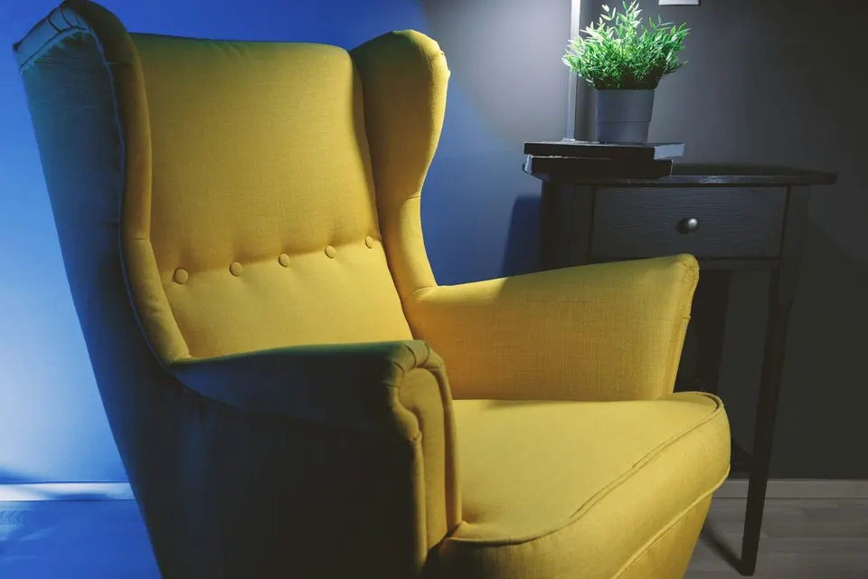 Gelber Ohrensessel mit Beistelltisch, Leselampe und Pflanze vor blauer Wand