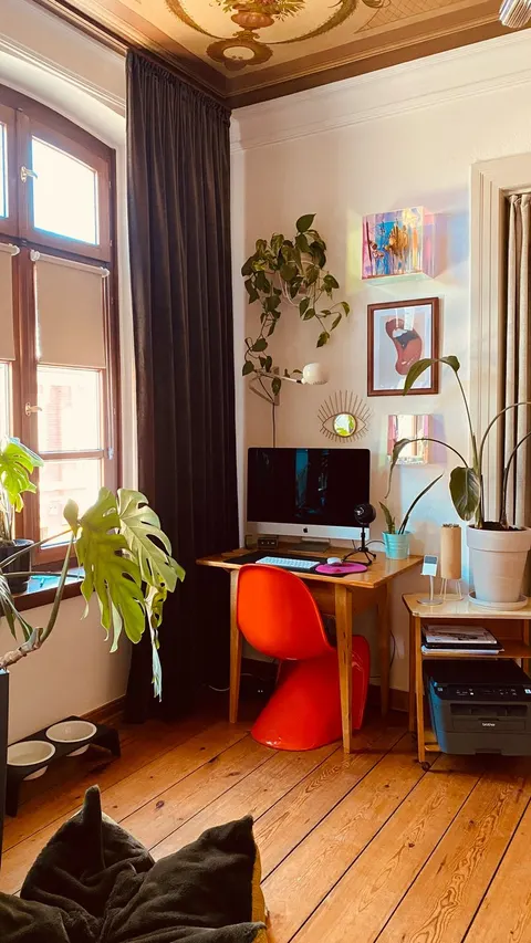 Roter Panton Chair an einem hölzernen Schreibtisch vor weißer Wand in einem Altbauzimmer, Licht fällt von der Seite durchs Fenster