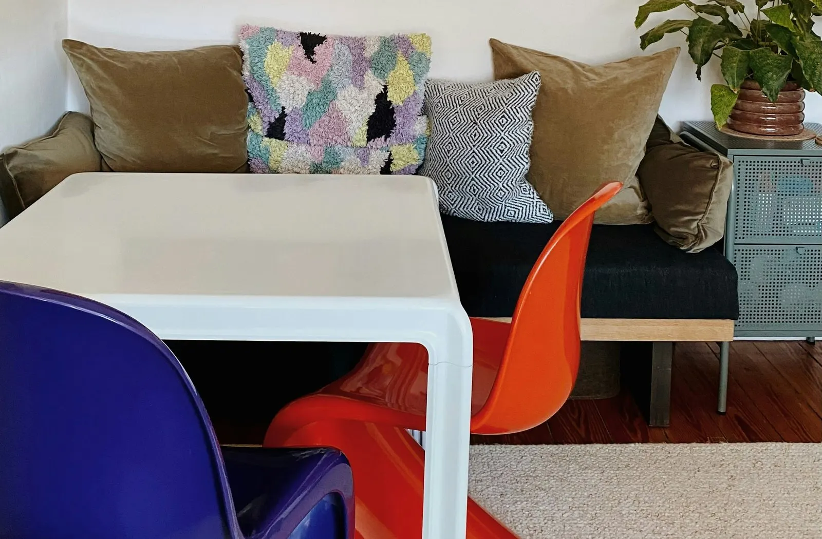 Drei Panton Chairs in Blau, Rot und Orange an einem weißen Esstisch, gegenüber eine gepolsterte Bank
