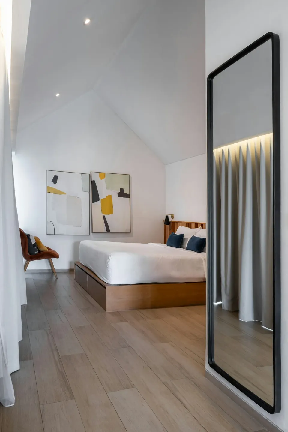 Schlafzimmer mit hohem schwarz gerahmtem Spiegel in der Zimmerecke neben Bett und Vorhang
