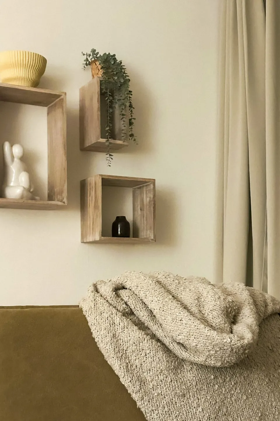 Drei offene Holzregale mit Pflanzen und Dekoration an einer hellen Wand über einem Sofa
