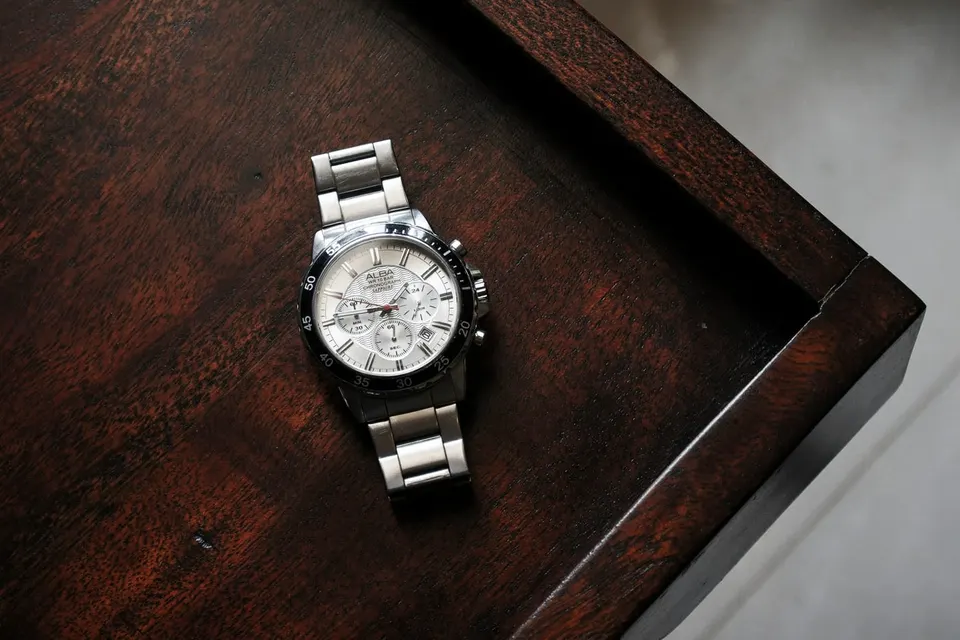 Silberner Chronograph mit Gliederband liegt auf einer dunklen Holzkommode