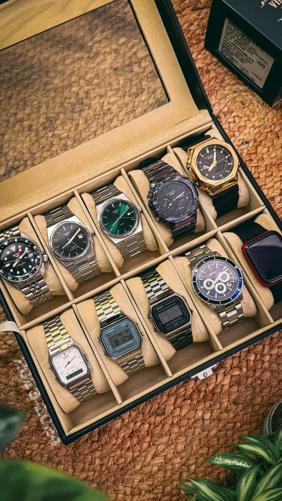 Geöffnete Uhrenbox mit zehn Fächern, darin Taucheruhr, Dresswatch, digitale Retro-Modelle und ein Chronograph auf hellen Kissen