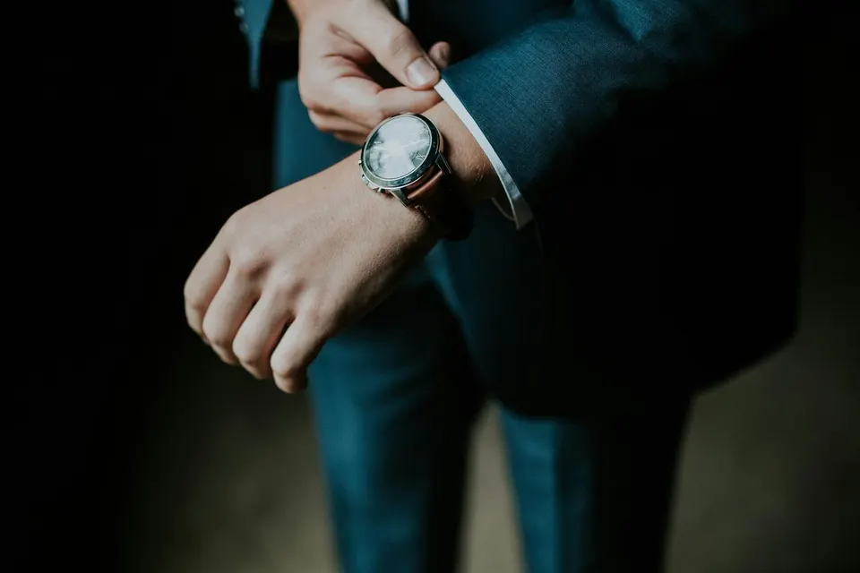 Mann im dunkelblauen Anzug richtet die Hemdmanschette, am Handgelenk eine Uhr mit braunem Lederband
