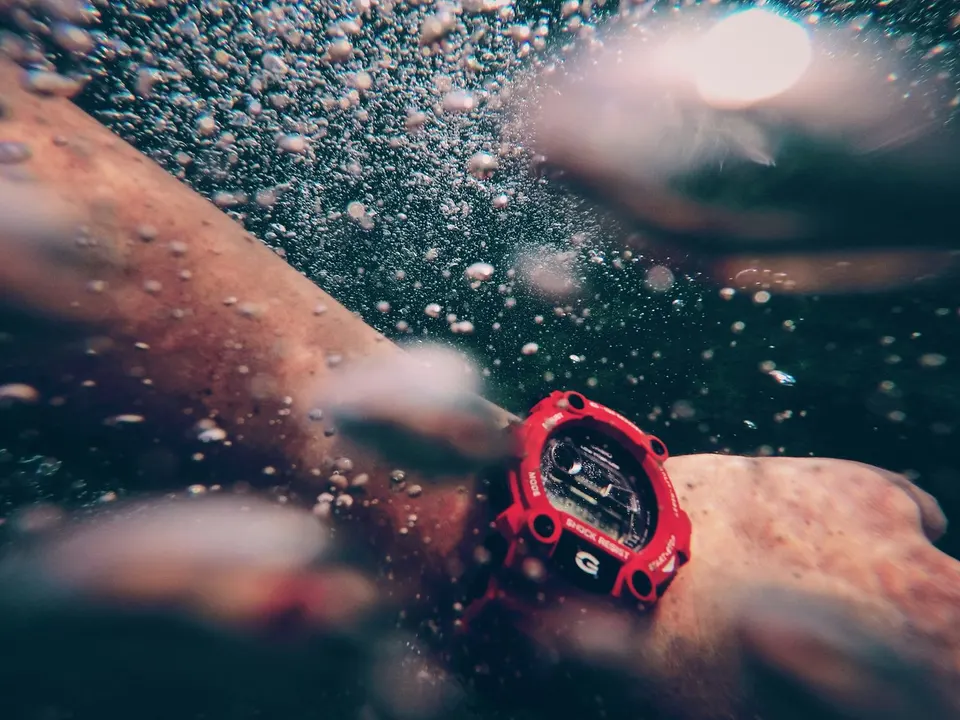 Arm mit robuster roter Digitaluhr unter Wasser, umgeben von aufsteigenden Luftblasen