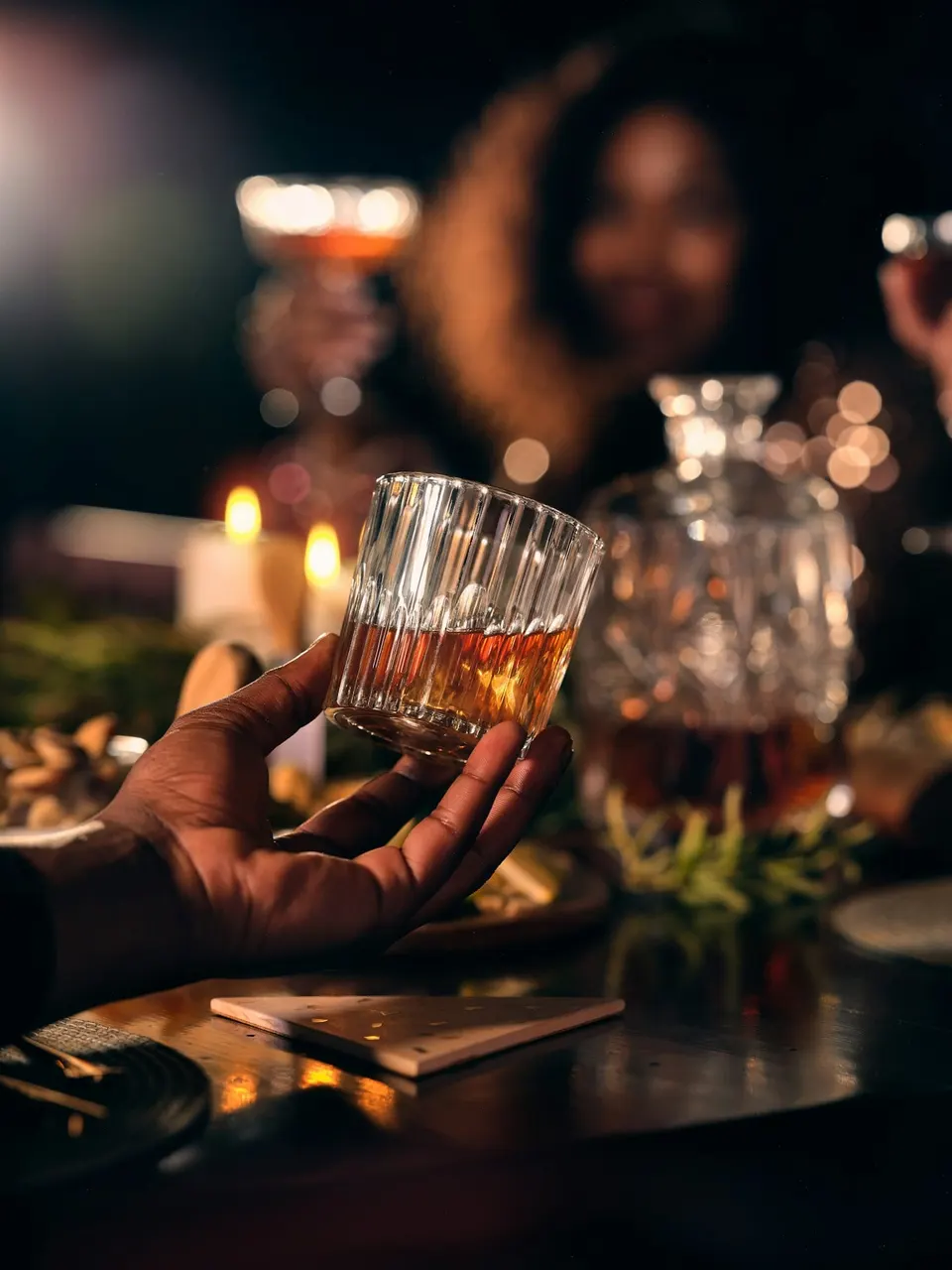 Hand hält ein tulpenförmiges Nosing-Glas mit Whisky vor dunklem Hintergrund