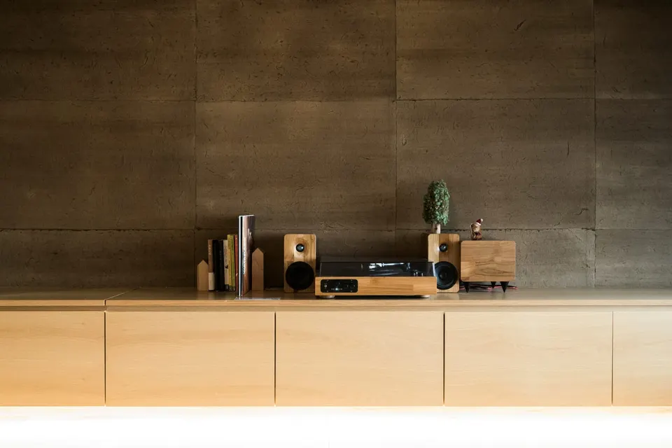 Kompakte Anlage mit zwei Holzlautsprechern auf einem langen hellen Sideboard vor einer dunklen Steinwand