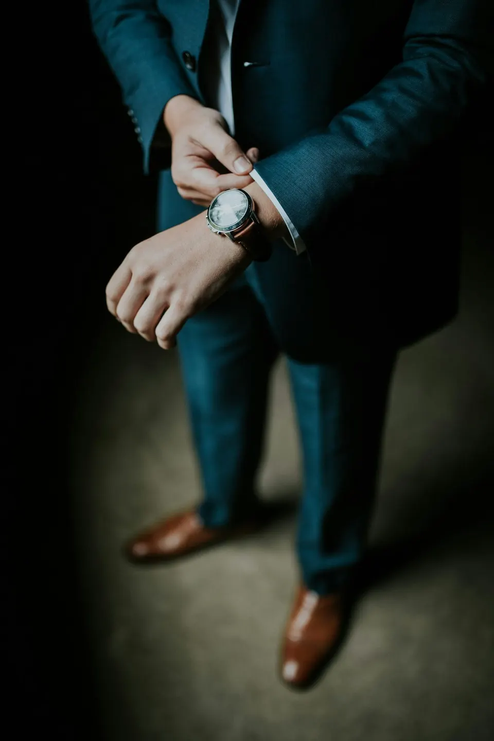 Mann im blauen Anzug richtet die Manschette, am Handgelenk eine klassische Uhr mit braunem Lederband